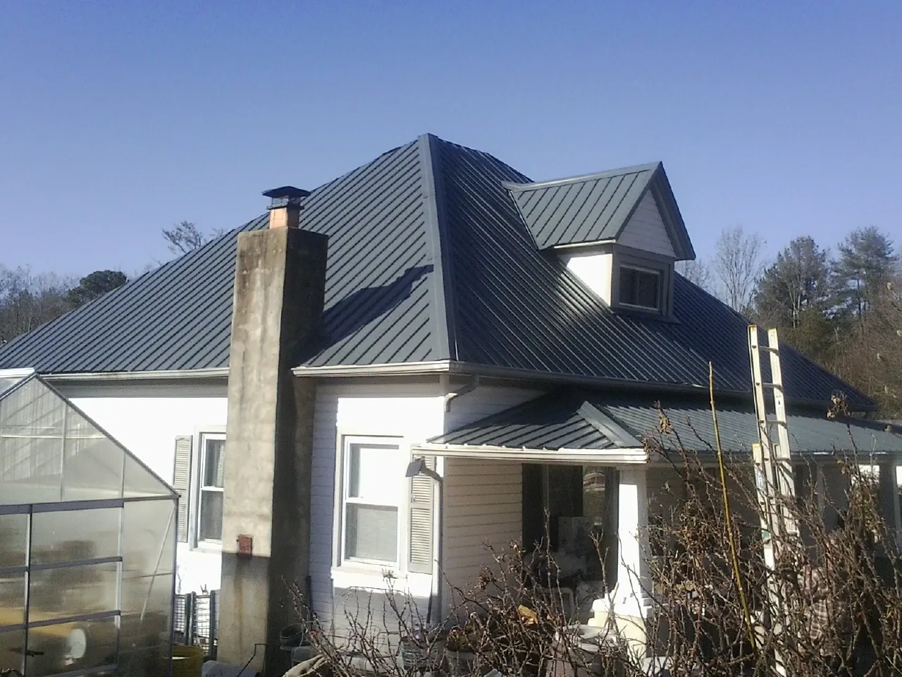 Dark blue standing seam metal roof on a white farmhouse with dormer — Slate & Tile Roof Repair by Roofing Brothers in Bartlesville