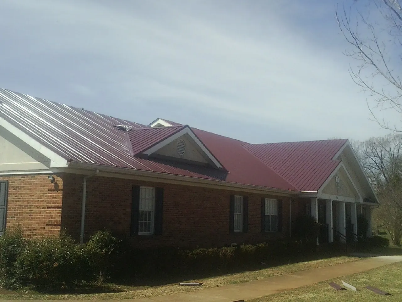 Red metal roof with gabled entries on a long brick building, from a Hail Damage Roof Repair job in Bartlesville