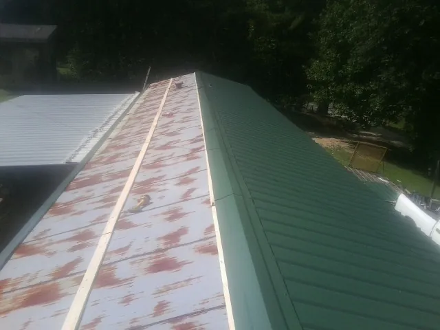 Old rusted panels beside newly installed green metal roofing — Wind Damage Roof Repair by Roofing Brothers in Bartlesville