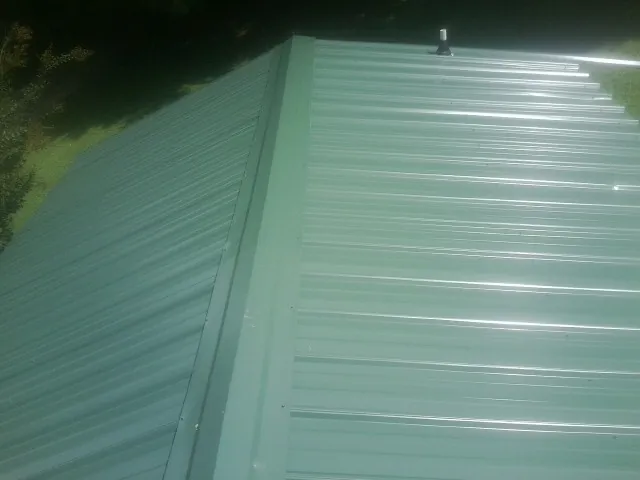 New green metal panels meeting at the ridge of a roof — Flat Roof Repair work by our crew in Bartlesville