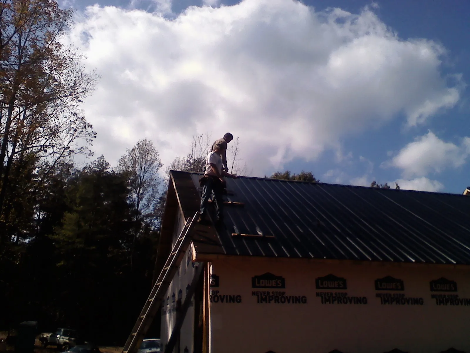 Roofer fastening dark metal panels high against a cloudy sky in Bartlesville