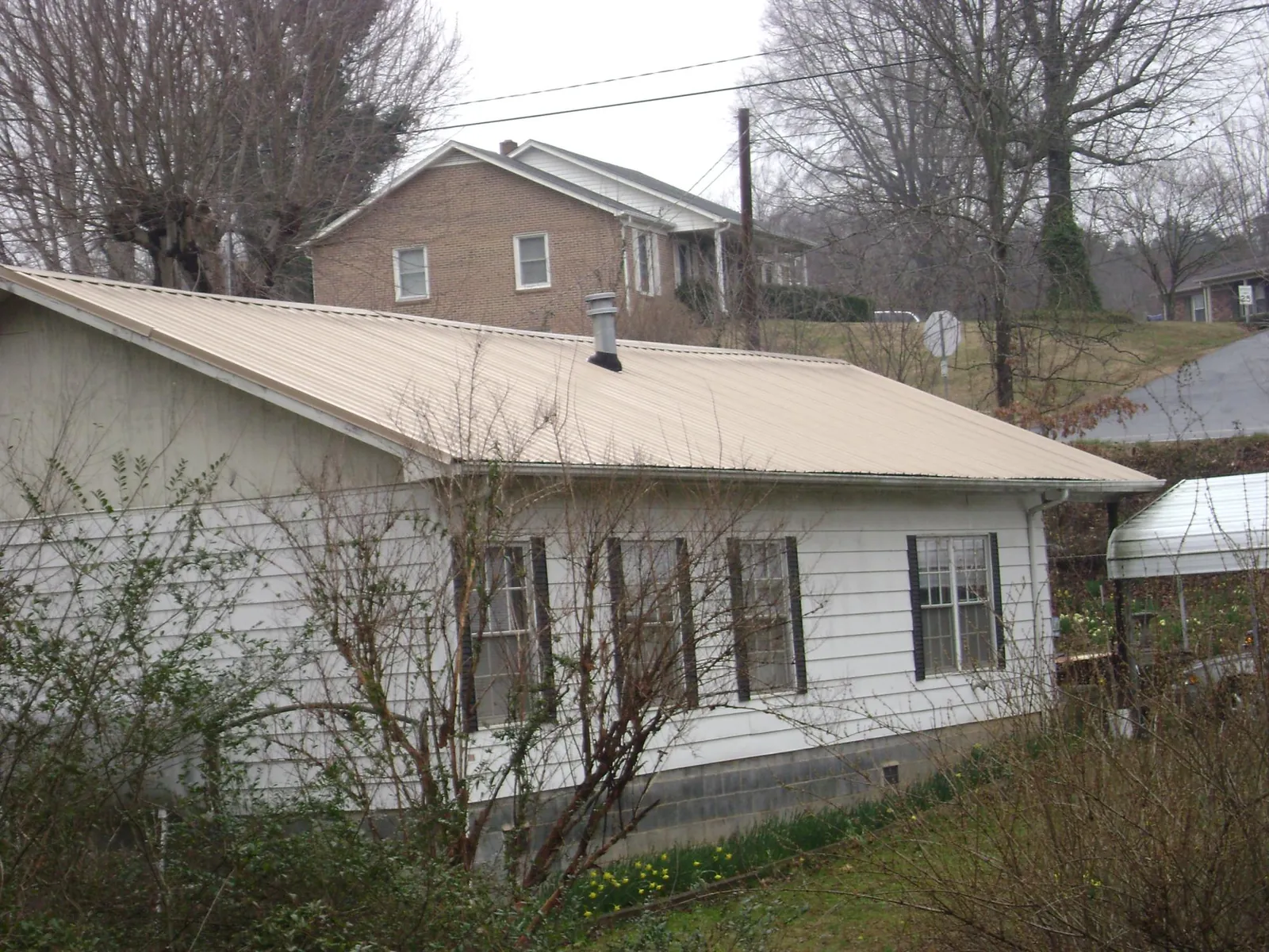 Tan metal roof on a white sided house set into a hillside — Commercial Roofing by Roofing Brothers in Bartlesville