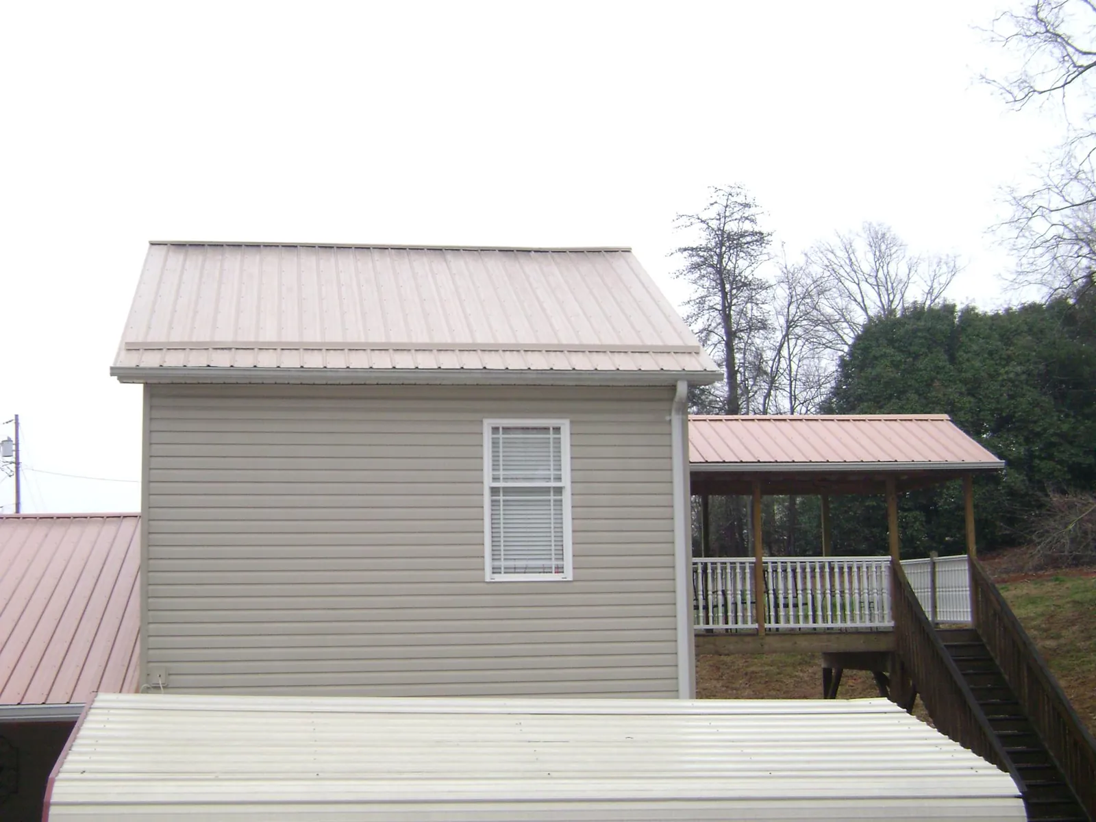 Tan metal roofs on a two story addition and attached porch, from a Roof Replacement job in Bartlesville