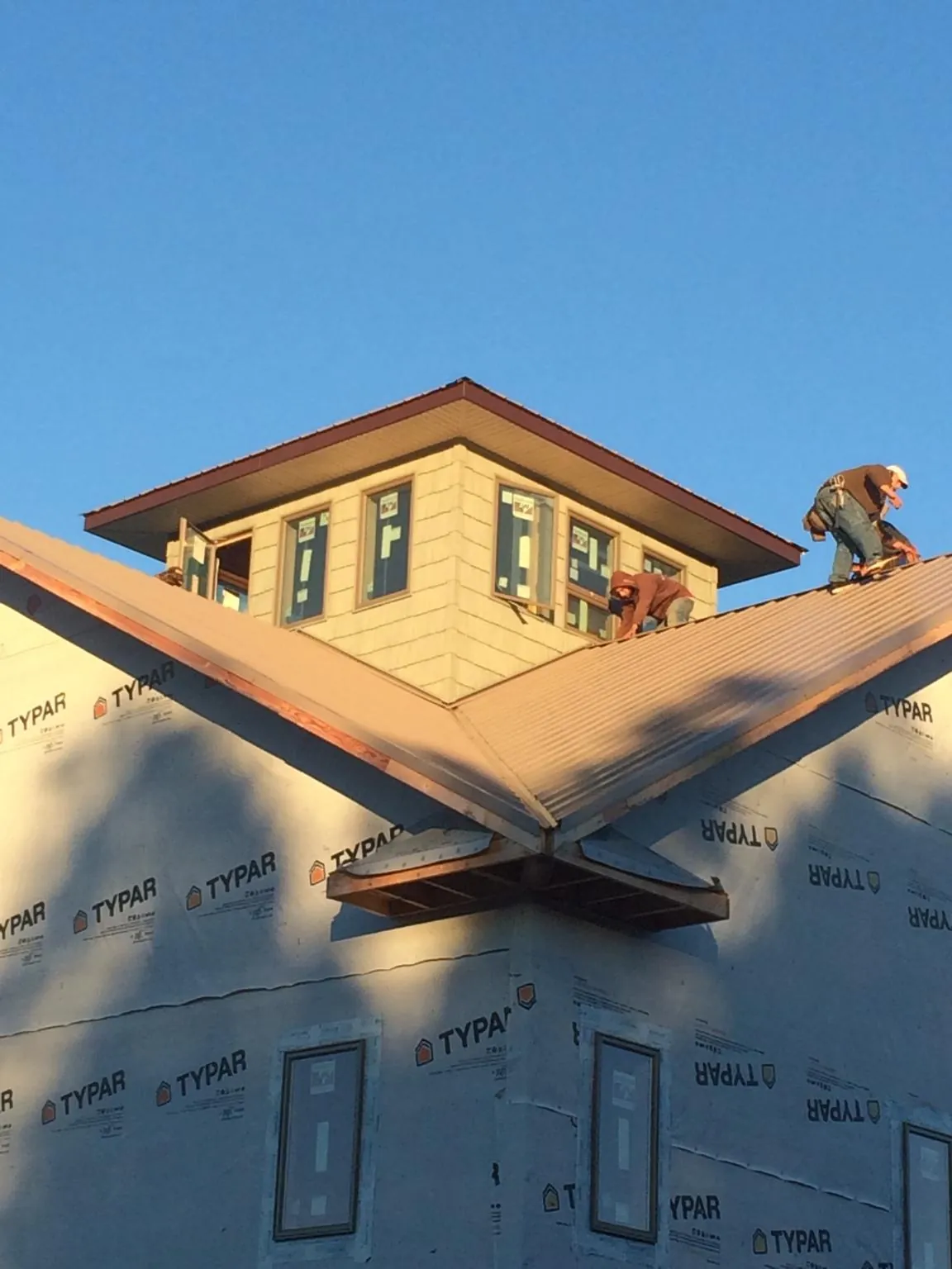 Roofers working around a rooftop cupola on a new metal roof at sunset — Roof Waterproofing in Bartlesville by Roofing Brothers